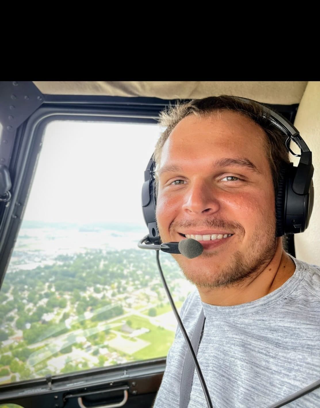 Frank Foust smiling in an aircraft, wearing a headset, with the ground visible through the window